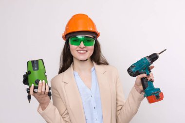 Turuncu kasklı ve ellerinde lazer seviyesinde beyaz bir arka plan olan bir kız..