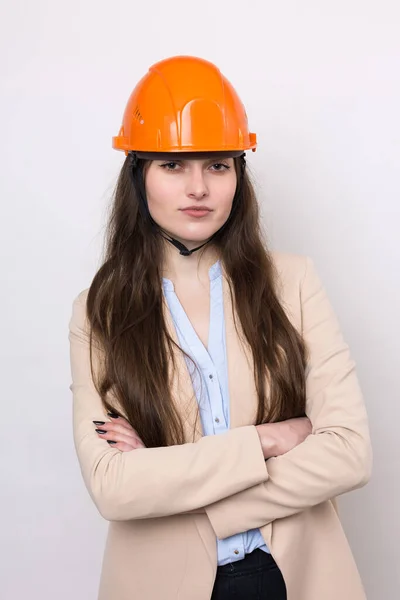 白い背景にはスーツ姿の少女建築家とオレンジの建設用ヘルメットが立っている — ストック写真