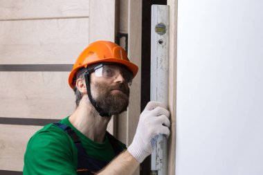 Erkek bir çilingir bir daireye kapı yerleştirir. Adam ölçümlerin doğruluğunu bina seviyesiyle kontrol ediyor..