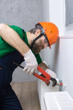Erkek bir tesisatçı bir apartmanın ısıtma sistemine radyatör yerleştiriyor. Tulumlu ve ingiliz anahtarı olan bir adam..