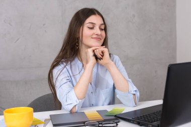 Masada oturan genç bir tasarımcı kız tablete resim çizer. Bilgisayarda iş hesaplamaları yapar.