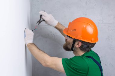 Bir elektrikçi daireye prizler takıyor. Turuncu kasklı ve tulumlu bir adam evde elektrik üretiyor..