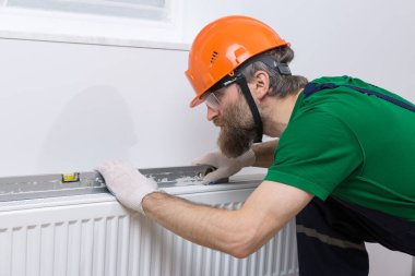 Erkek bir tesisatçı bir apartmanın ısıtma sistemine radyatör yerleştiriyor. Tulumlu ve ingiliz anahtarı olan bir adam..