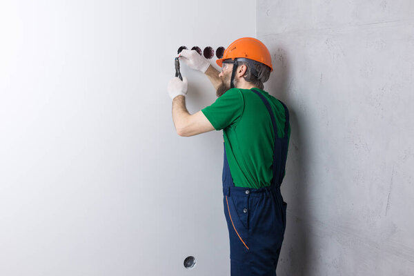 An electrician installs sockets in the apartment. A guy in an orange helmet and overalls makes electrics in the house.