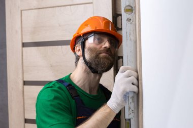 Erkek bir çilingir bir daireye kapı yerleştirir. Adam ölçümlerin doğruluğunu bina seviyesiyle kontrol ediyor..
