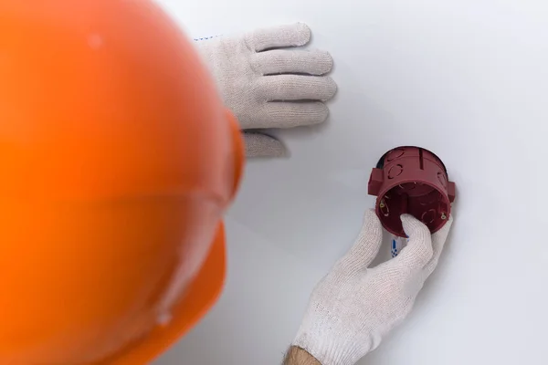 電気技師はアパートにソケットをインストールします オレンジのヘルメットの男と全体は家の中で電気を作る — ストック写真