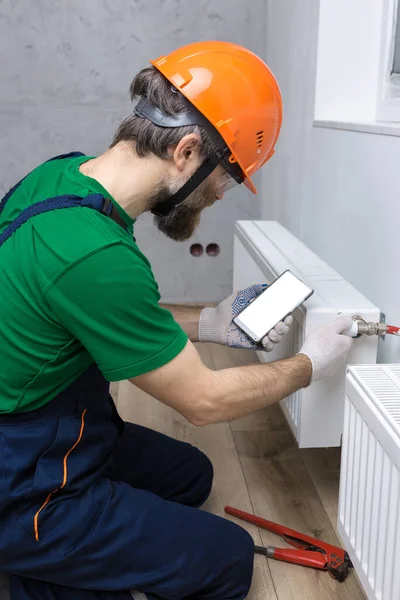 Manlig Rörmokare Installerar Kylare Värmesystemet Lägenhet Killen Tittar Telefoninstruktionerna Mokap — Stockfoto
