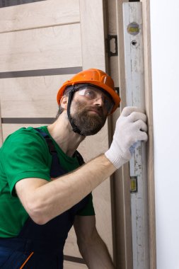 Erkek bir çilingir bir daireye kapı yerleştirir. Adam ölçümlerin doğruluğunu bina seviyesiyle kontrol ediyor..