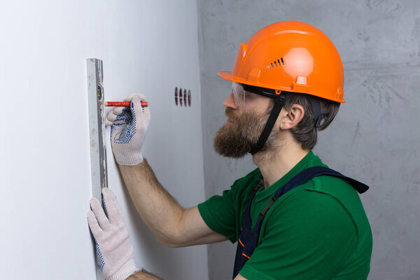An electrician installs sockets in the apartment. A guy in an orange helmet and overalls makes electrics in the house.