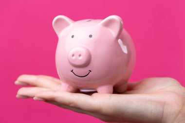 Pembe ceketli şirin bir kız elinde 3 boyutlu bir kumbara tutuyor. Stüdyoda pembe üzerine yakın plan güzel bir portre.