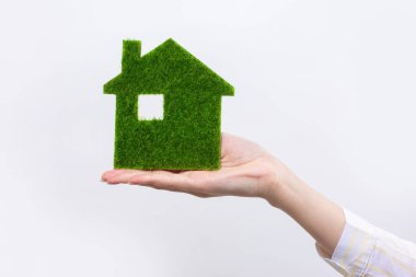 Kadın eli, yakın plan bir yeşil evin modelini tutuyor. Geleceğin ekolojik gayrimenkullerinin satışı.