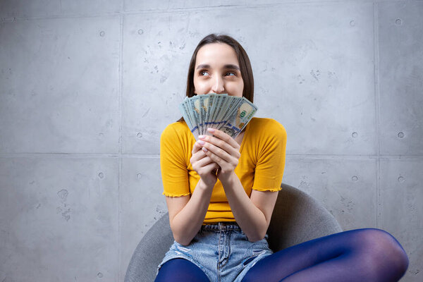Фото богатой женщины в простой одежде, держащей фаната долларовых денег, изолированных на фоне бетонной стены