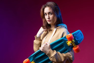 Kapüşonlu güzel, modaya uygun hippi kız elinde mor bir stüdyo geçmişiyle kaykayı tutuyor..