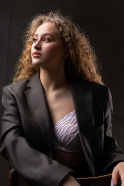 Stüdyoda uzun saçlı, ceketli, kızıl saçlı, kıvırcık bir kızın portresi. Koyu renkli dramatik fotoğraf.