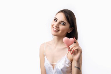 Temiz ciltli, doğal makyajlı ve gri arka planda beyaz dişli güzel bir kadın. Pembe hijyenik bir kalp taşıyor..