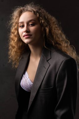 Stüdyoda uzun saçlı, ceketli, kızıl saçlı, kıvırcık bir kızın portresi. Koyu renkli dramatik fotoğraf.