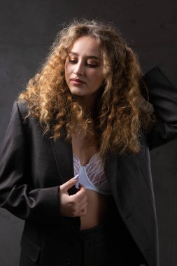 Stüdyoda uzun saçlı, ceketli, kızıl saçlı, kıvırcık bir kızın portresi. Koyu renkli dramatik fotoğraf.