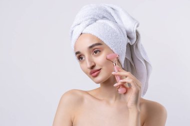 Kalın kaşlı güzel bir kız, beyaz arka planda mükemmel bir ten, kafasında havlu, güzel bir fotoğraf. Kozmetik rulo tutuyor..