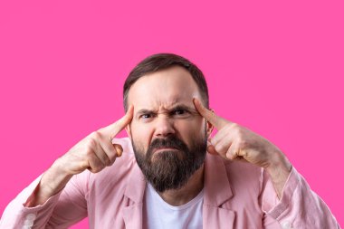 Pembe ceketli sakallı yakışıklı adam, izole edilmiş kırmızı bir arka plan düşünüyor..