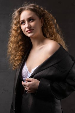 Stüdyoda uzun saçlı, ceketli, kızıl saçlı, kıvırcık bir kızın portresi. Kıvrımlı göğüslerini sütyen içinde gösteriyor..