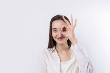 Beyaz stüdyo arka planında güzel bir jest sergileyen ve elleriyle dürbün yapan çekici genç kadının portresini kapat..