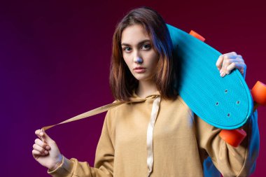 Kapüşonlu güzel, modaya uygun hippi kız elinde mor bir stüdyo geçmişiyle kaykayı tutuyor..