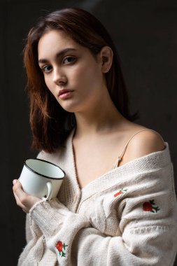 Stüdyoda uzun saçlı genç bir esmerin portresi. Kızın elinde beyaz bir kupa var..