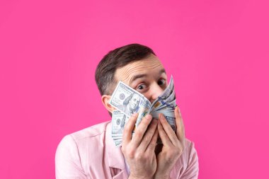 Pembe ceketli sakallı, mutlu genç bir iş adamının portresi kırmızı bir stüdyonun arka planında bize dolar banknotları gösteriyor. Tat, para kokusu..