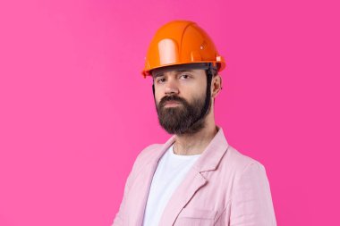 Genç inşaat mühendisinin portresi kırmızı stüdyo arka planında duran pembe ceketli turuncu bir şapka giyer..