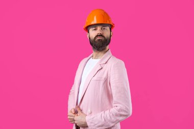 Genç inşaat mühendisinin portresi kırmızı stüdyo arka planında duran pembe ceketli turuncu bir şapka giyer..