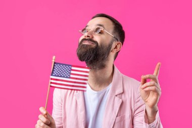 Kırmızı stüdyo arka planında Amerikan bayrağı olan sakallı, memnun bir gencin portresi. Büyük ABD vatansever ve özgürlüğün savunucusu.