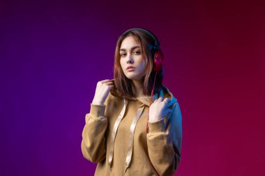 Kapüşonlu giyinmiş, kırmızı kulaklıklı, stüdyo kırmızı dramatik bir arka planda müzik dinleyen güzel, modaya uygun bir hippi kız.