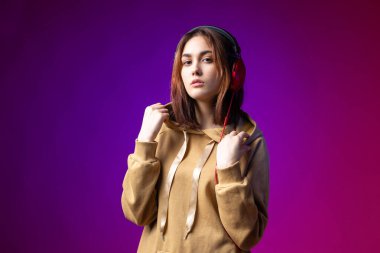 Kapüşonlu giyinmiş, kırmızı kulaklıklı, stüdyo kırmızı dramatik bir arka planda müzik dinleyen güzel, modaya uygun bir hippi kız.