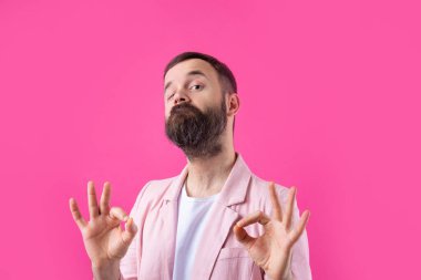 Pembe ceketli gülümseyen genç bir adamın portresi. İzole edilmiş kırmızı arka planda stüdyoda dikilirken iyi niyet gösteren bir adam.