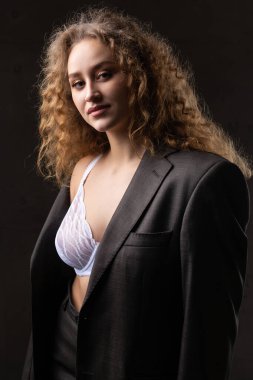 Stüdyoda uzun saçlı, ceketli, kızıl saçlı, kıvırcık bir kızın portresi. Kıvrımlı göğüslerini sütyen içinde gösteriyor..