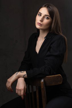 Stüdyoda uzun saçlı genç bir esmerin portresi. Koyu renkli dramatik bir fotoğraf. Kolunda yılan dövmesi olan bir kız..