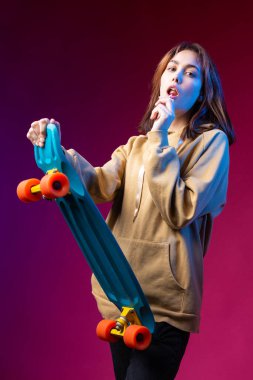 Kapüşonlu güzel, modaya uygun bir hippi kız elinde mor bir stüdyo geçmişiyle bir kaykay tutuyor. Lolipop yiyor..