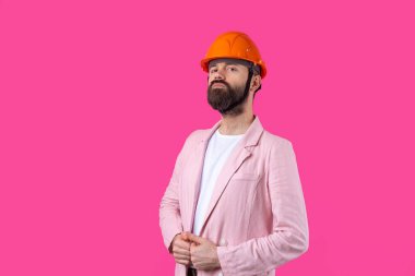 Genç inşaat mühendisinin portresi kırmızı stüdyo arka planında duran pembe ceketli turuncu bir şapka giyer..