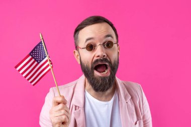 Kırmızı stüdyo arka planında Amerikan bayrağı olan sakallı, memnun bir gencin portresi. Büyük ABD vatansever ve özgürlüğün savunucusu.