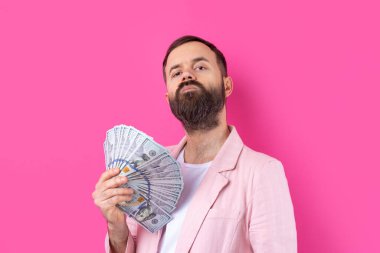 Pembe ceketli sakallı, mutlu genç bir iş adamının portresi kırmızı bir stüdyonun arka planında bize dolar banknotları gösteriyor. Tat, para kokusu..