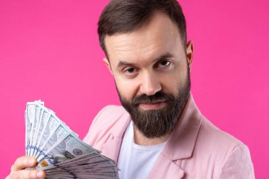 Pembe ceketli sakallı, mutlu genç bir iş adamının portresi kırmızı bir stüdyonun arka planında bize dolar banknotları gösteriyor. Tat, para kokusu..