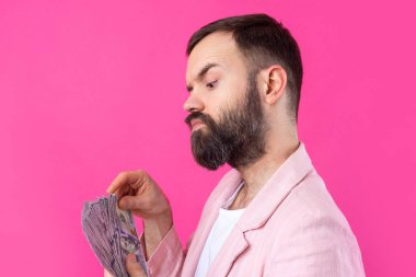 Pembe ceketli sakallı, mutlu genç bir iş adamının portresi kırmızı bir stüdyonun arka planında bize dolar banknotları gösteriyor. Tat, para kokusu..