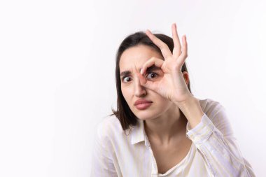 Beyaz stüdyo arka planında güzel bir jest sergileyen ve elleriyle dürbün yapan çekici genç kadının portresini kapat..