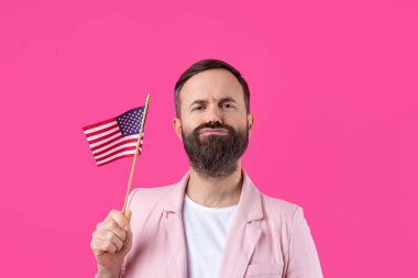Kırmızı stüdyo arka planında Amerikan bayrağı olan sakallı, memnun bir gencin portresi. Büyük ABD vatansever ve özgürlüğün savunucusu.