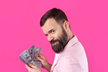 Pembe ceketli sakallı, mutlu genç bir iş adamının portresi kırmızı bir stüdyonun arka planında bize dolar banknotları gösteriyor. Tat, para kokusu..