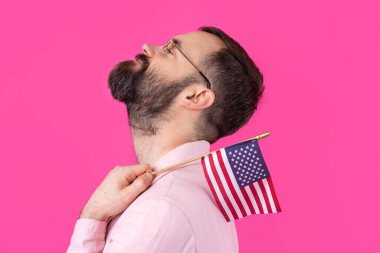 Kırmızı stüdyo arka planında Amerikan bayrağı olan sakallı, memnun bir gencin portresi. Büyük ABD vatansever ve özgürlüğün savunucusu.