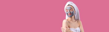 Pasifiğin pembe arka planında beyaz havluyla gri kozmetik maskeli bir kadın..