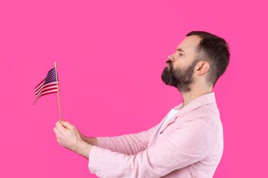 Kırmızı stüdyo arka planında Amerikan bayrağı olan sakallı, memnun bir gencin portresi. Büyük ABD vatansever ve özgürlüğün savunucusu.