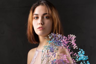 Zarif, çıplak bir beden giymiş güzel seksi bir bayan elinde çiçekler tutuyor. Moda mankeni kızın güzel portresi stüdyoda..