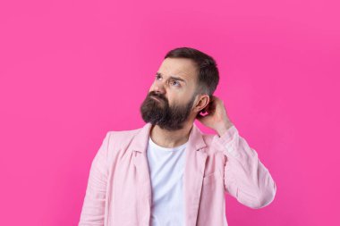 Pembe ceketli sakallı yakışıklı adam, izole edilmiş kırmızı bir arka plan düşünüyor..